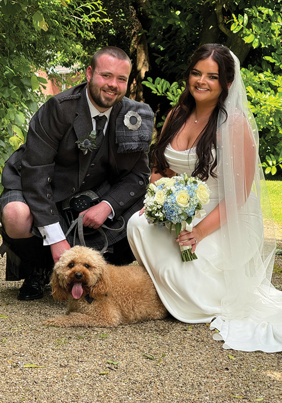 Bride and groom crouched down smile with dog